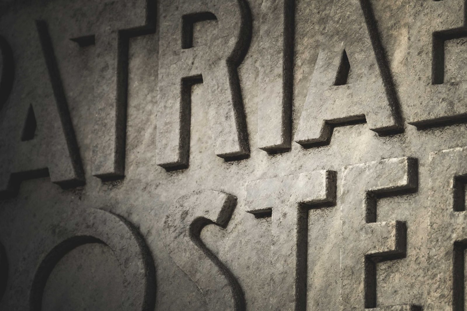 Close-up of large letters carved in relief on a grey stone wall